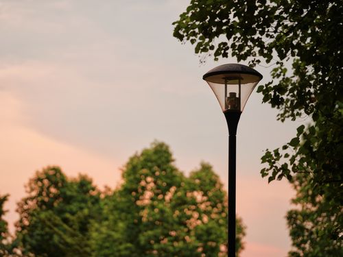 Free A tranquil scene with a streetlight silhouetted against a pastel sunset sky and lush trees. Stock Photo