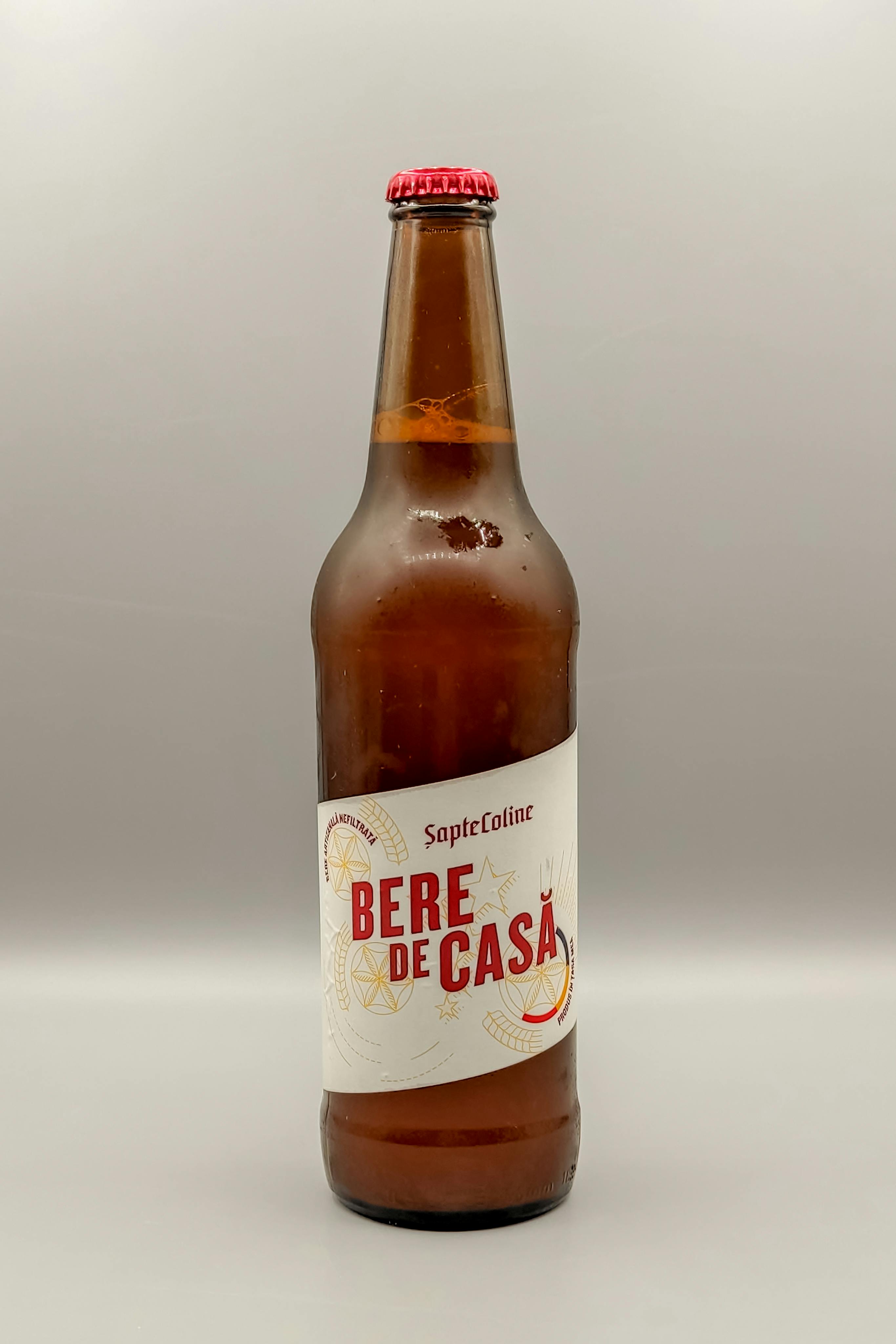 A clear view of a craft beer bottle labeled 'Bere de Casă' from Románia, on a white background.