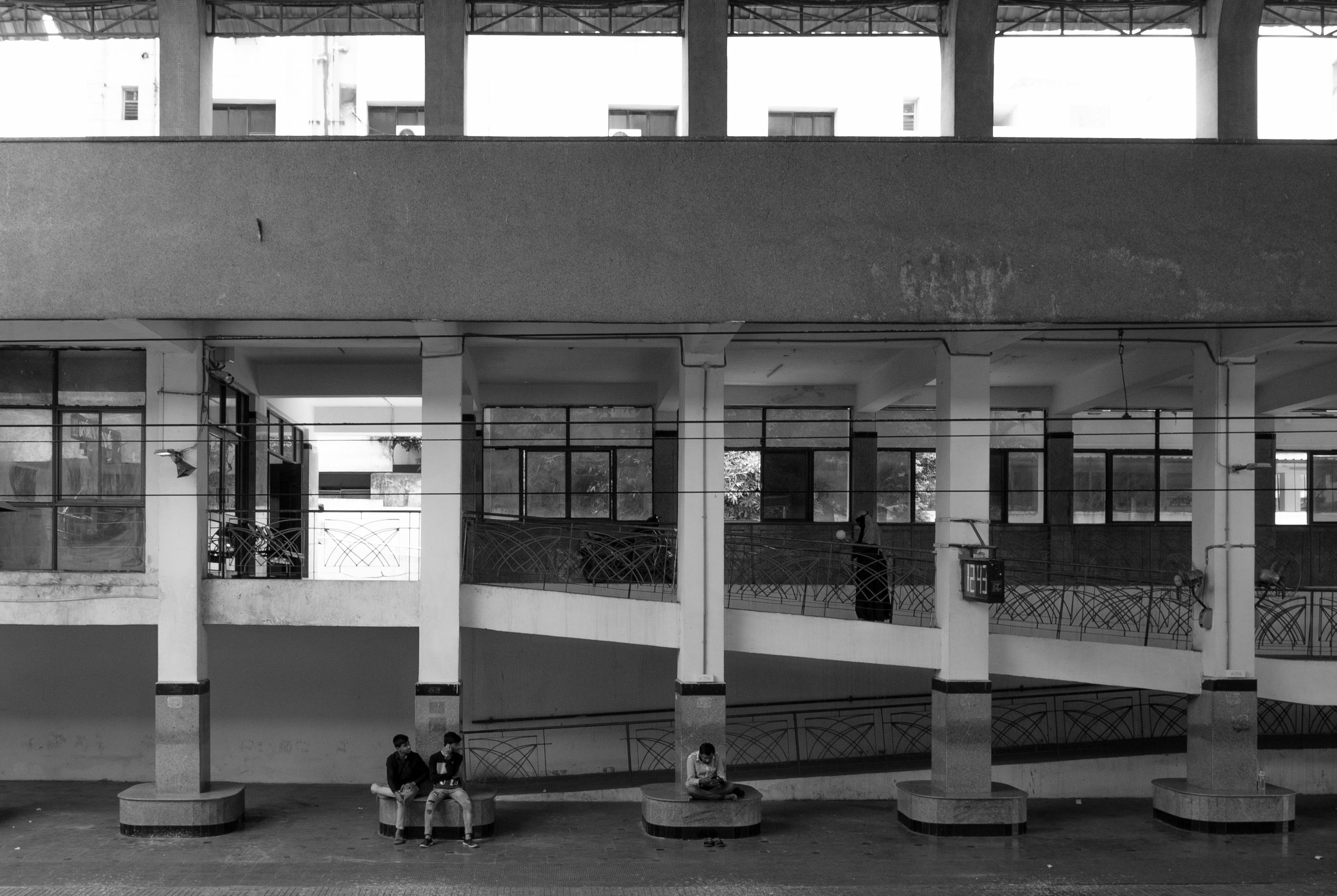 Monochrome shot of an elevated interior with people seated, depicting urban life.