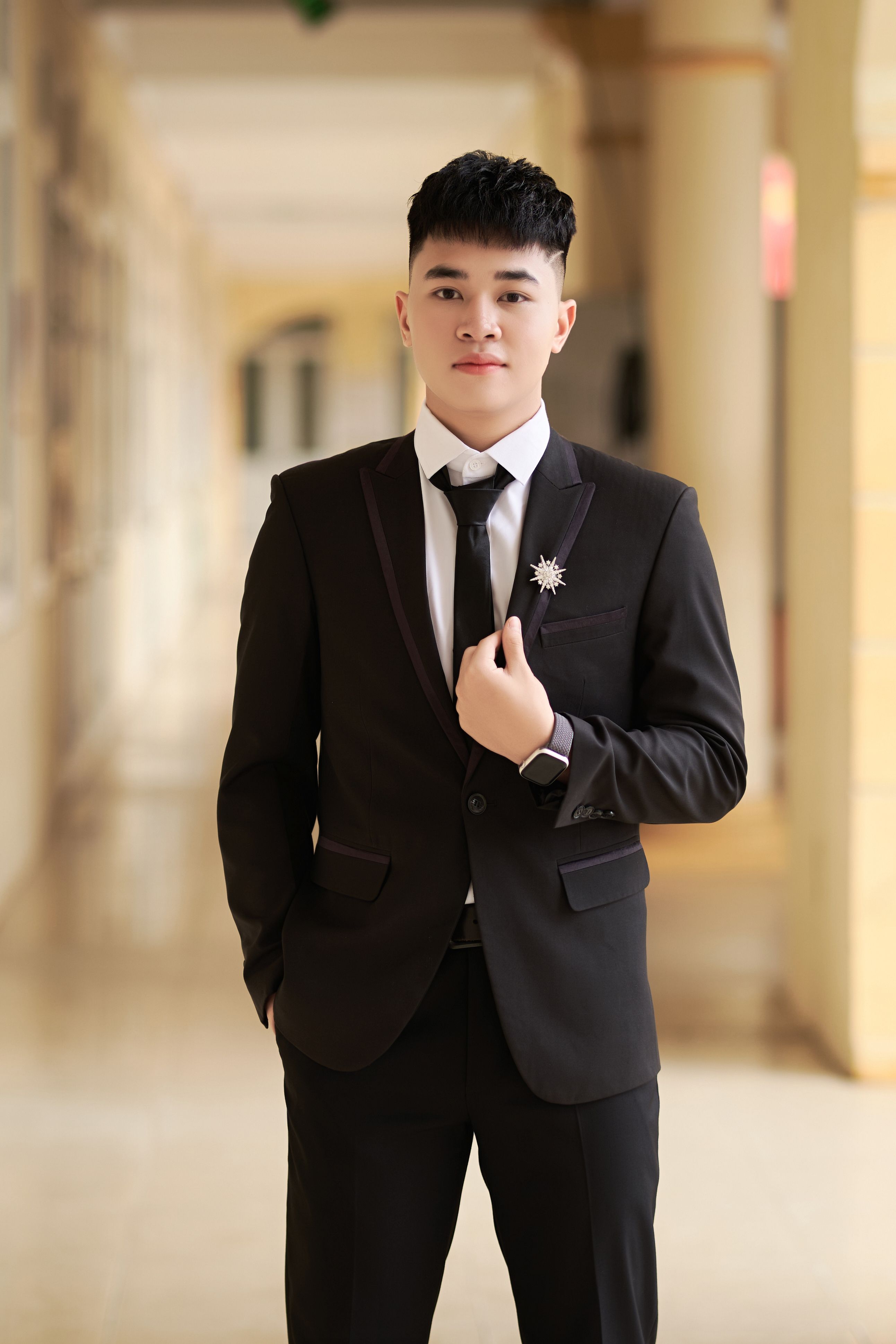 Well-dressed young man in a formal black suit standing confidently indoors, enhancing elegance.