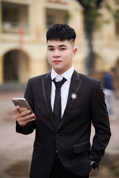 Confident young man in formal suit using smartphone in an outdoor setting.