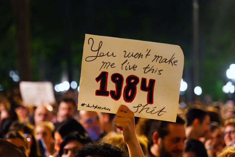 Crowd in Tbilisi holds a sign referencing Orwell's 1984 during a protest expressing dissent.