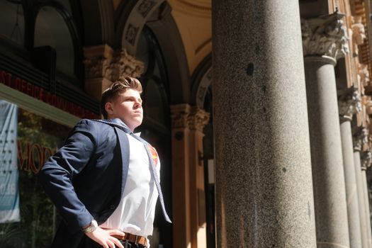 A determined man in a blue suit poses heroically outdoors under bright sunlight in Sydney, Australia.