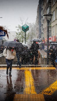 Pedestrians with umbrellas navigate a bustling city street during rainfall, showcasing urban life in adverse weather.