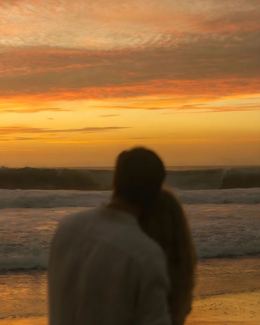 A couple embraces on a serene California beach at sunset, capturing romance and tranquility.