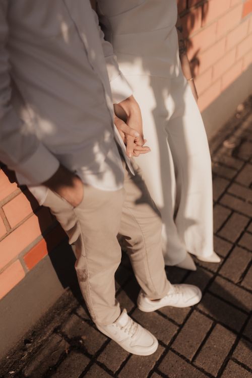 Free A couple holding hands facing a brick wall, casting soft shadows. Stock Photo