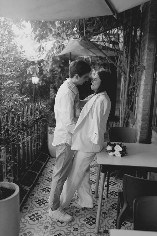 Free A couple shares a romantic moment outdoors under patio umbrellas next to a floral bouquet on the table. Stock Photo