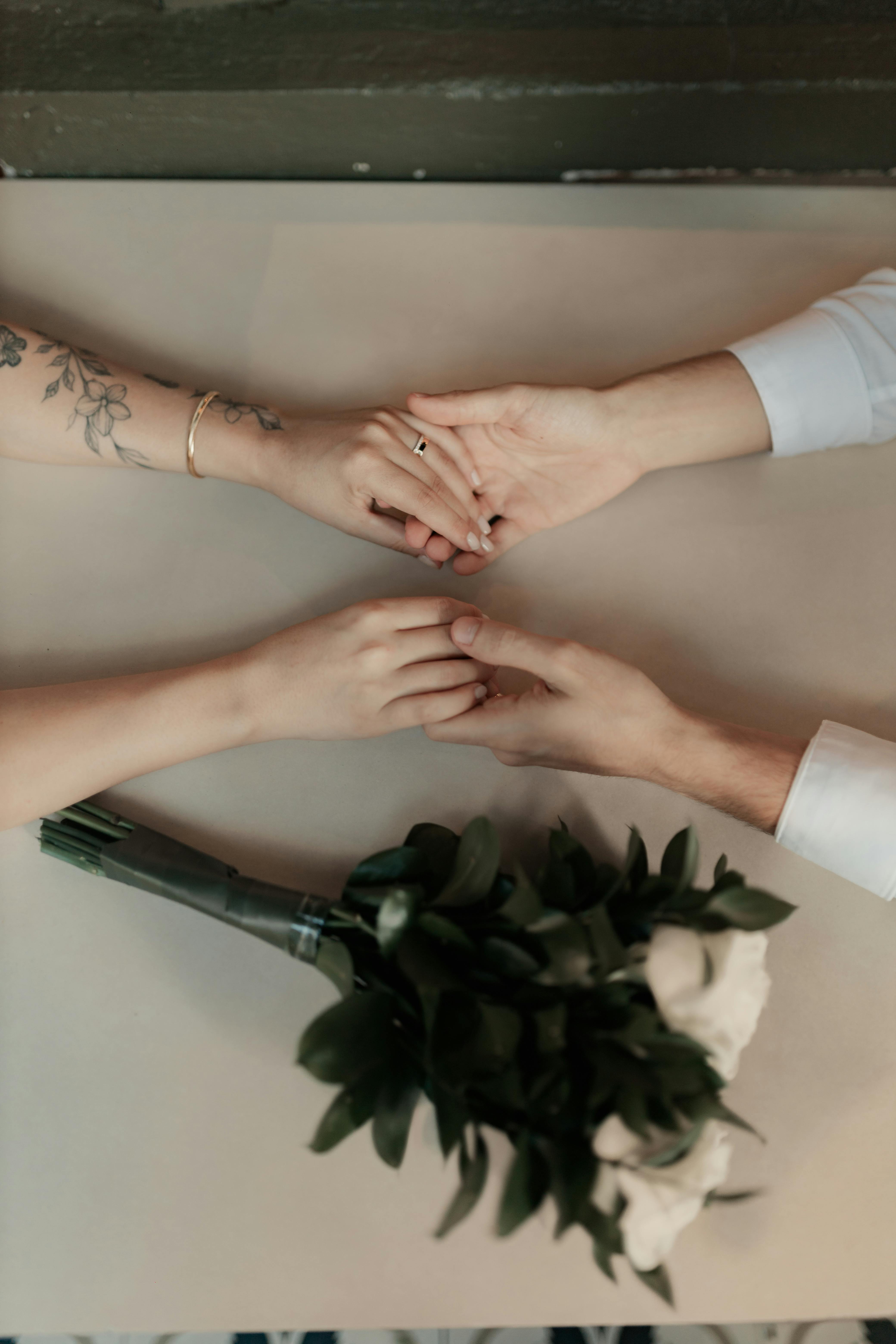 Безкоштовне Пара крупним планом тримається за руки з букетом, який символізує любов і відданість. стокове фото