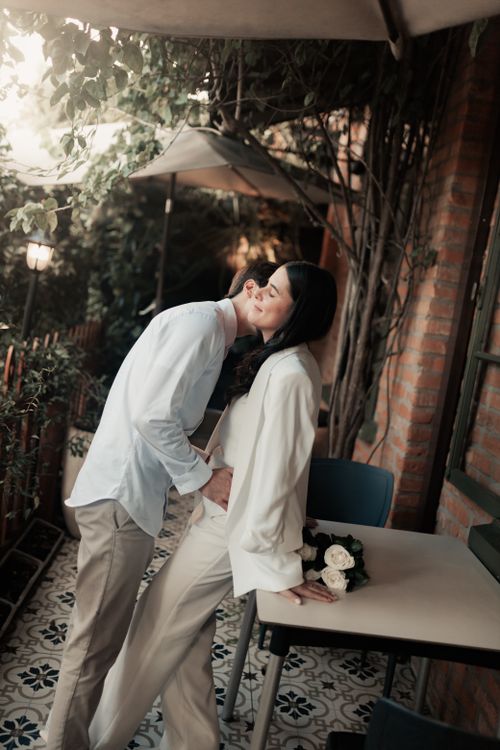 Free Romantic couple embrace on a charming outdoor patio adorned with flowers. Stock Photo