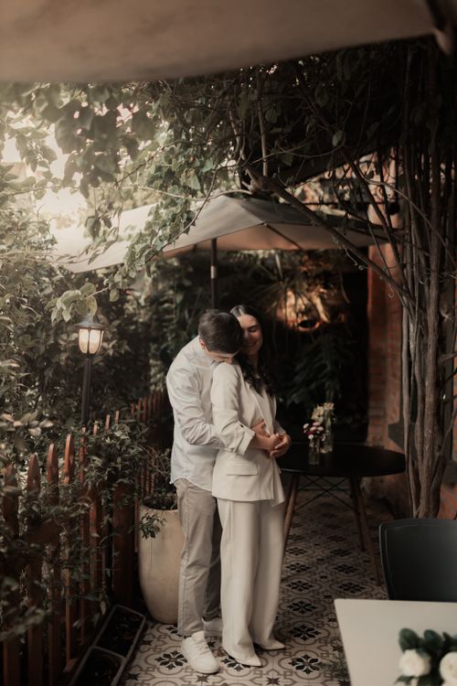 Free Couple embracing in a cozy, elegantly lit outdoor patio surrounded by lush greenery. Stock Photo