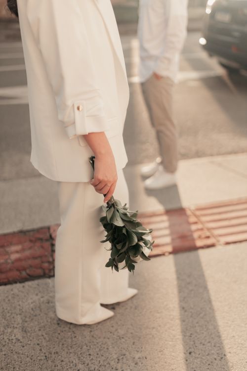 Free Chic woman in white attire holding a bouquet of greenery outdoors on a sunny day. Stock Photo
