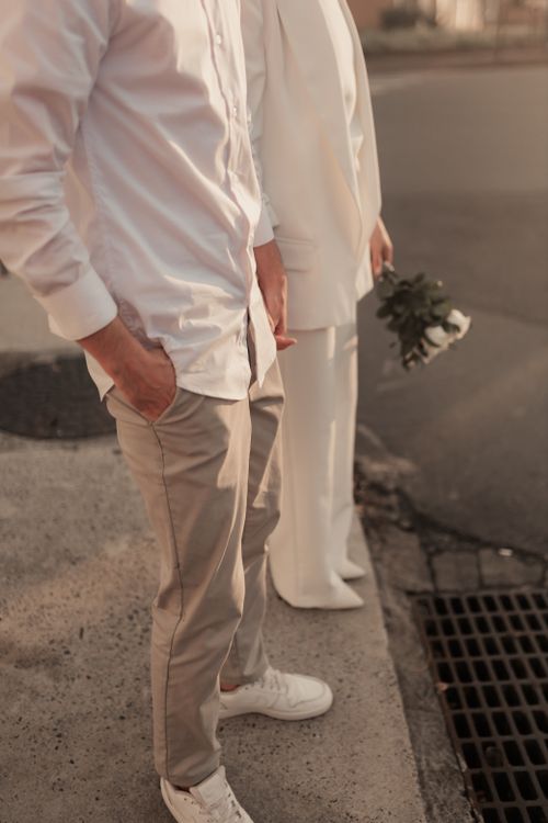 Free Couple in casual wedding attire standing on a city sidewalk, holding a bouquet. Stock Photo