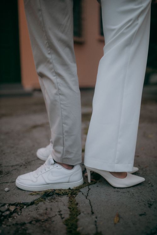 Free Close-up of legs in sneakers and high heels standing back-to-back on concrete pavement. Stock Photo