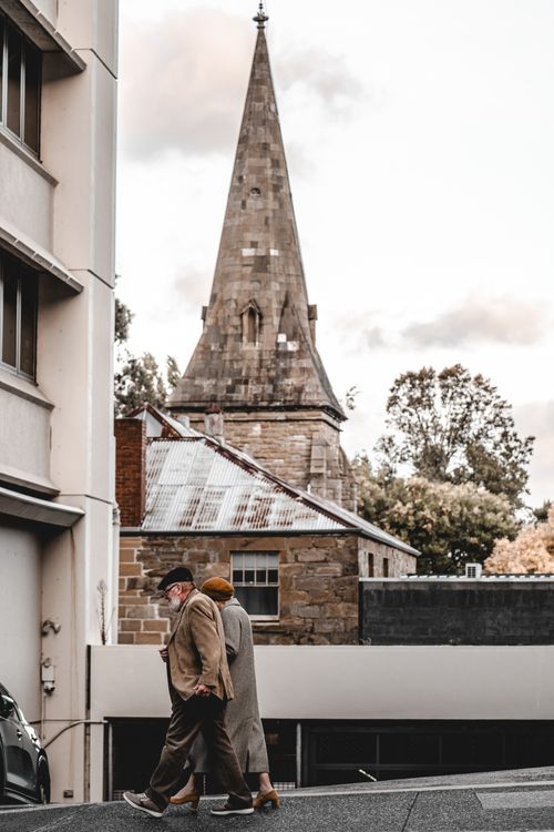 Free An elderly couple walks down the street with a historic stone church in the background. Stock Photo
