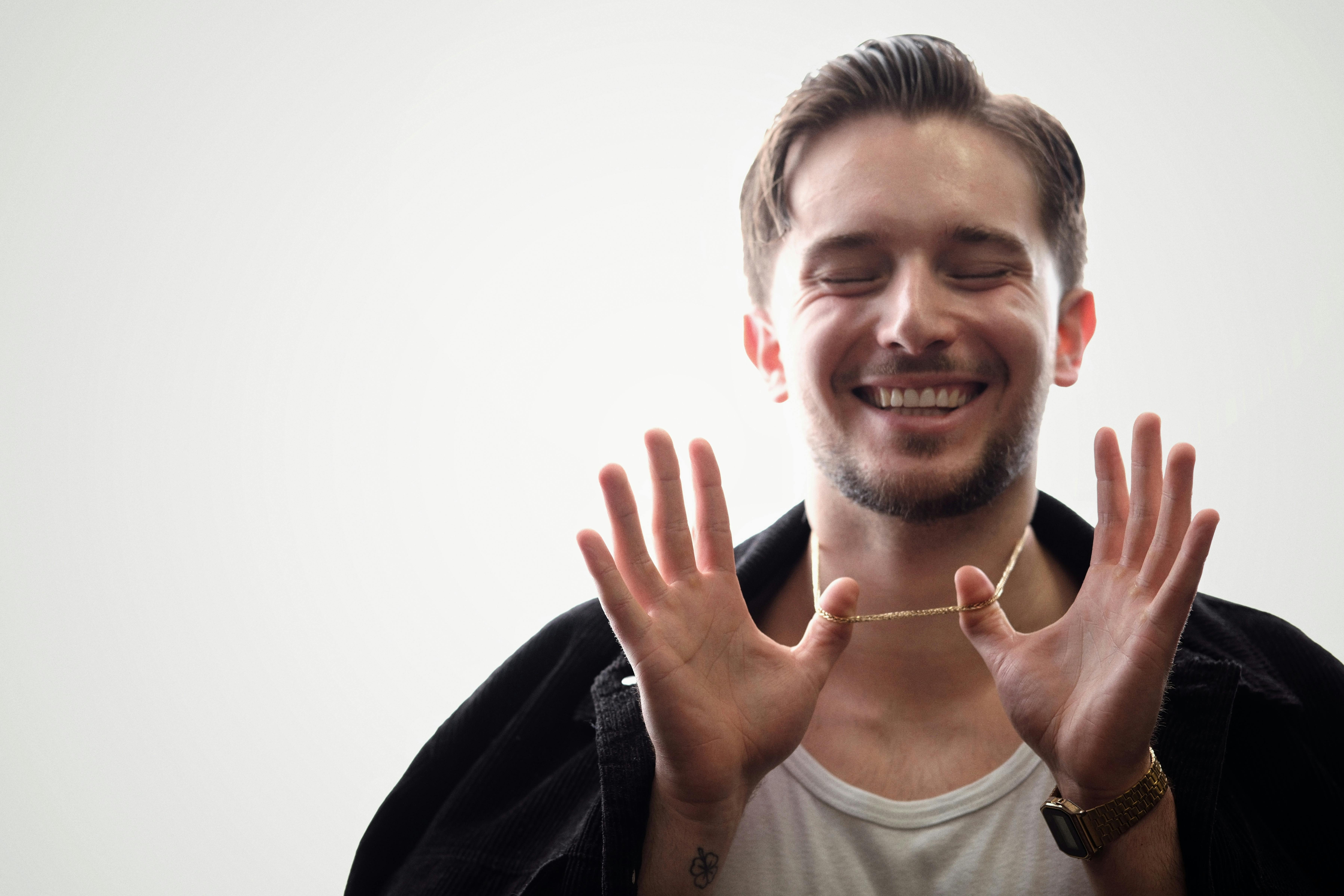 De franc Jove feliç amb els ulls tancats que mostra una cadena d'or sobre un fons clar. Foto d'estoc