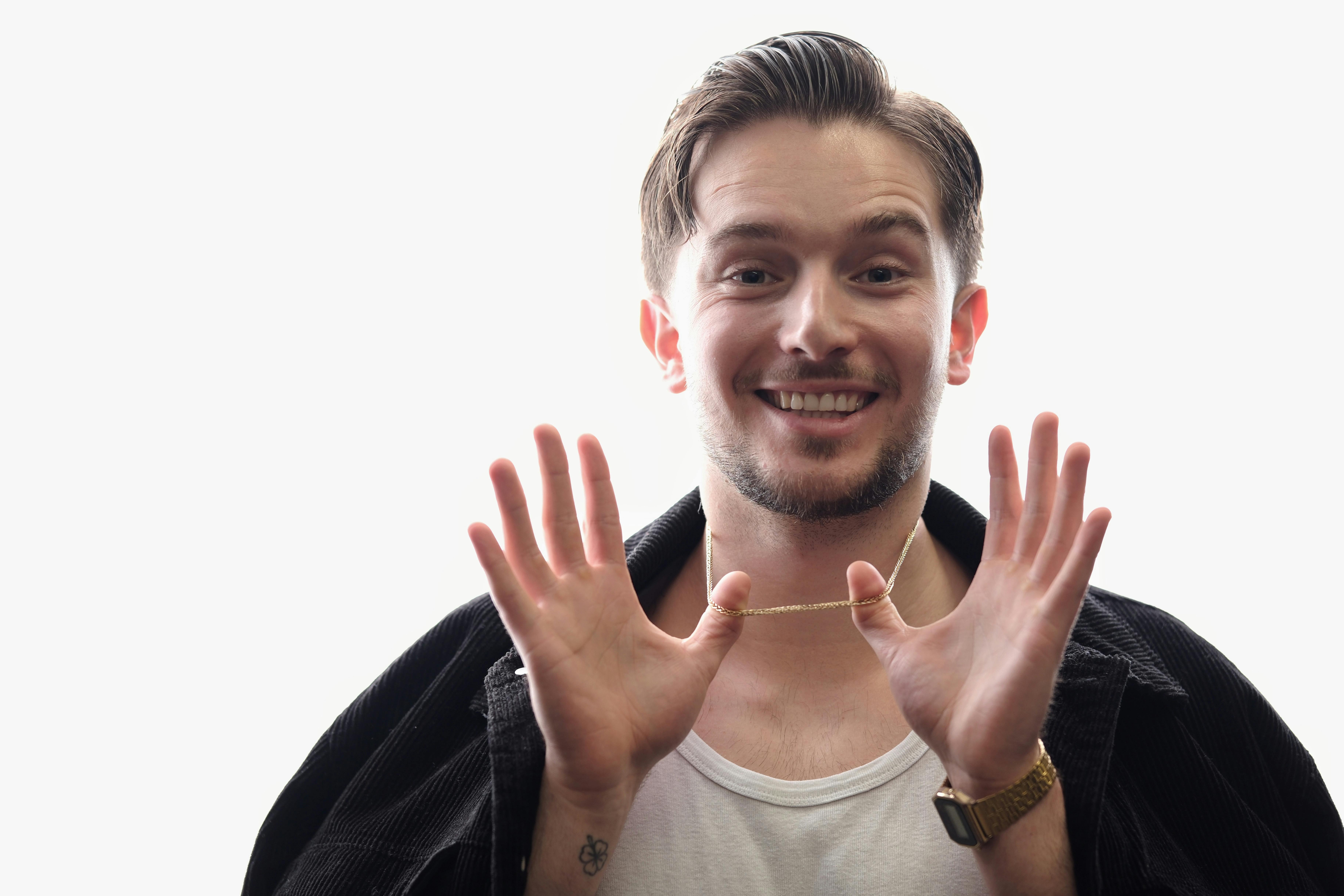 Gratis Un uomo felice mostra la sua collana con una posa allegra in un ambiente interno. Foto a disposizione