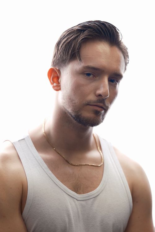 Free A young man poses in a white tank top with a confident look against a neutral background. Stock Photo