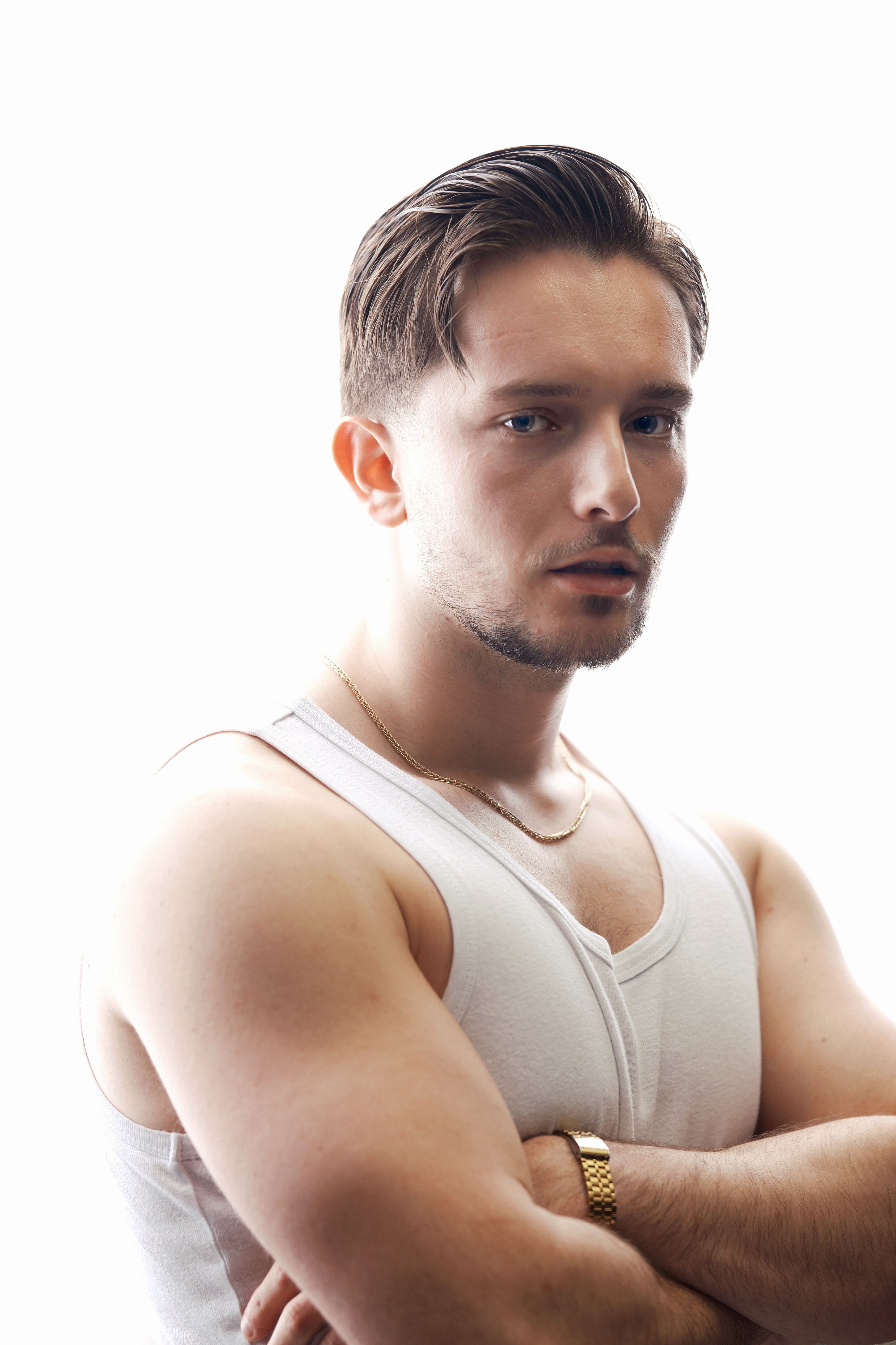 Portrait of a confident adult male in a white tank top, with arms crossed and direct gaze.