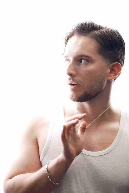 Free A young man in a white tank top is illuminated by bright light, looking pensive. Stock Photo