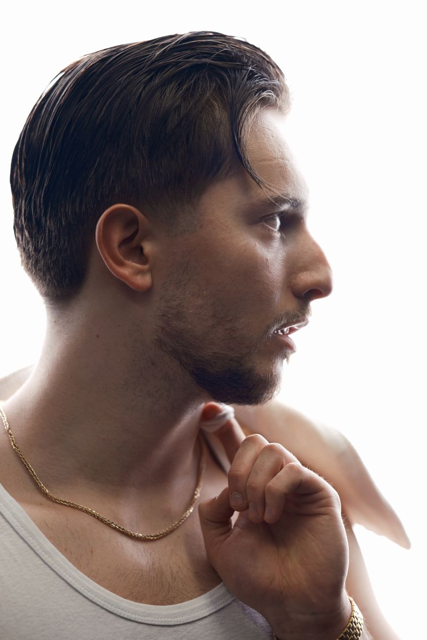 Side profile portrait of a young man in a white tank top and gold chain.