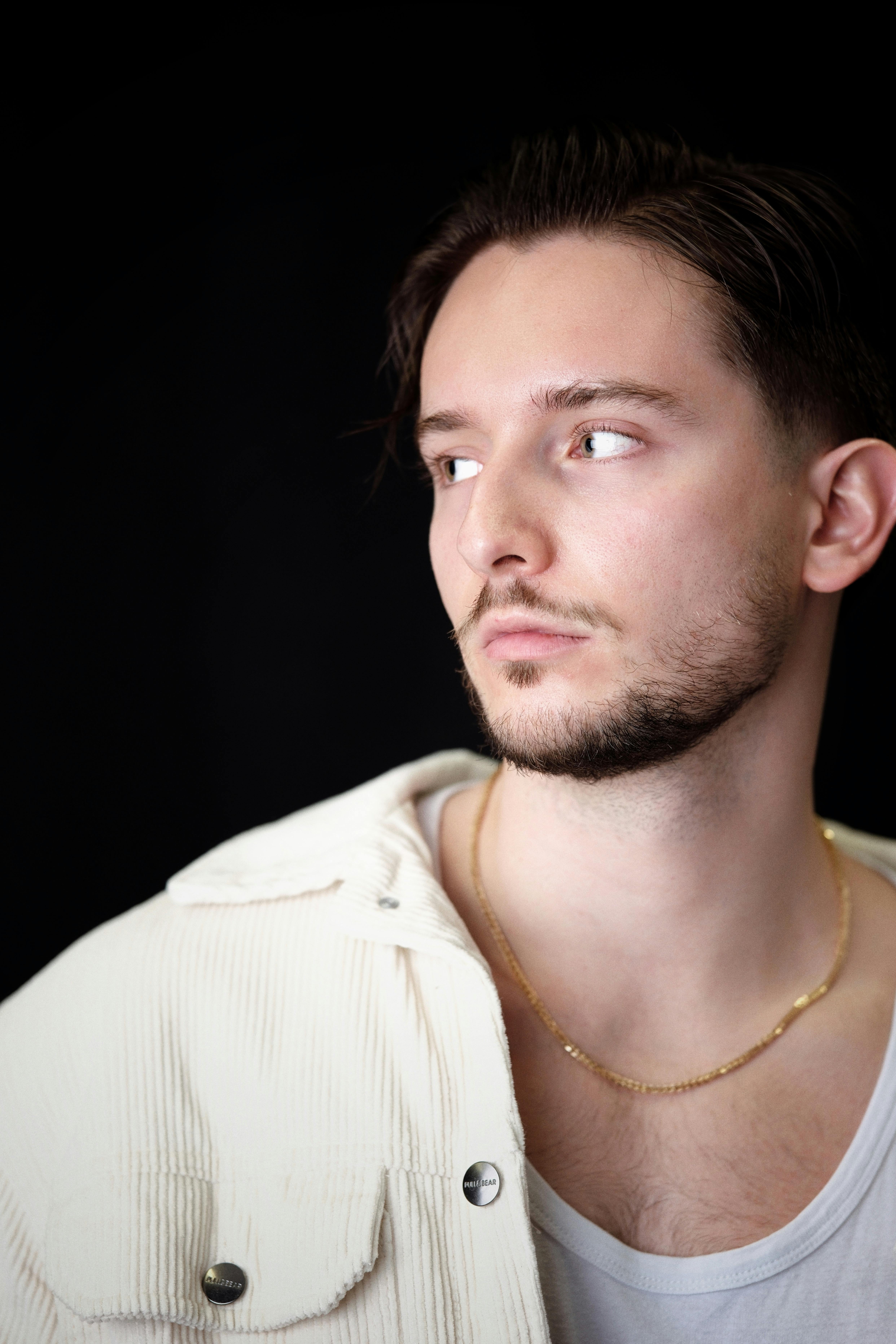 Young man looking away in thoughtful pose against dark background.