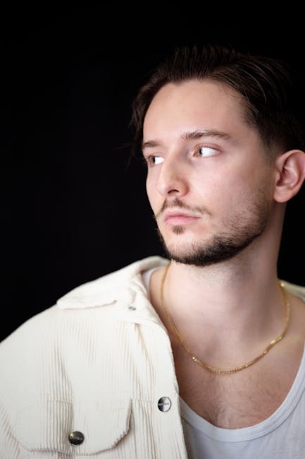 Young man looking away in thoughtful pose against dark background.