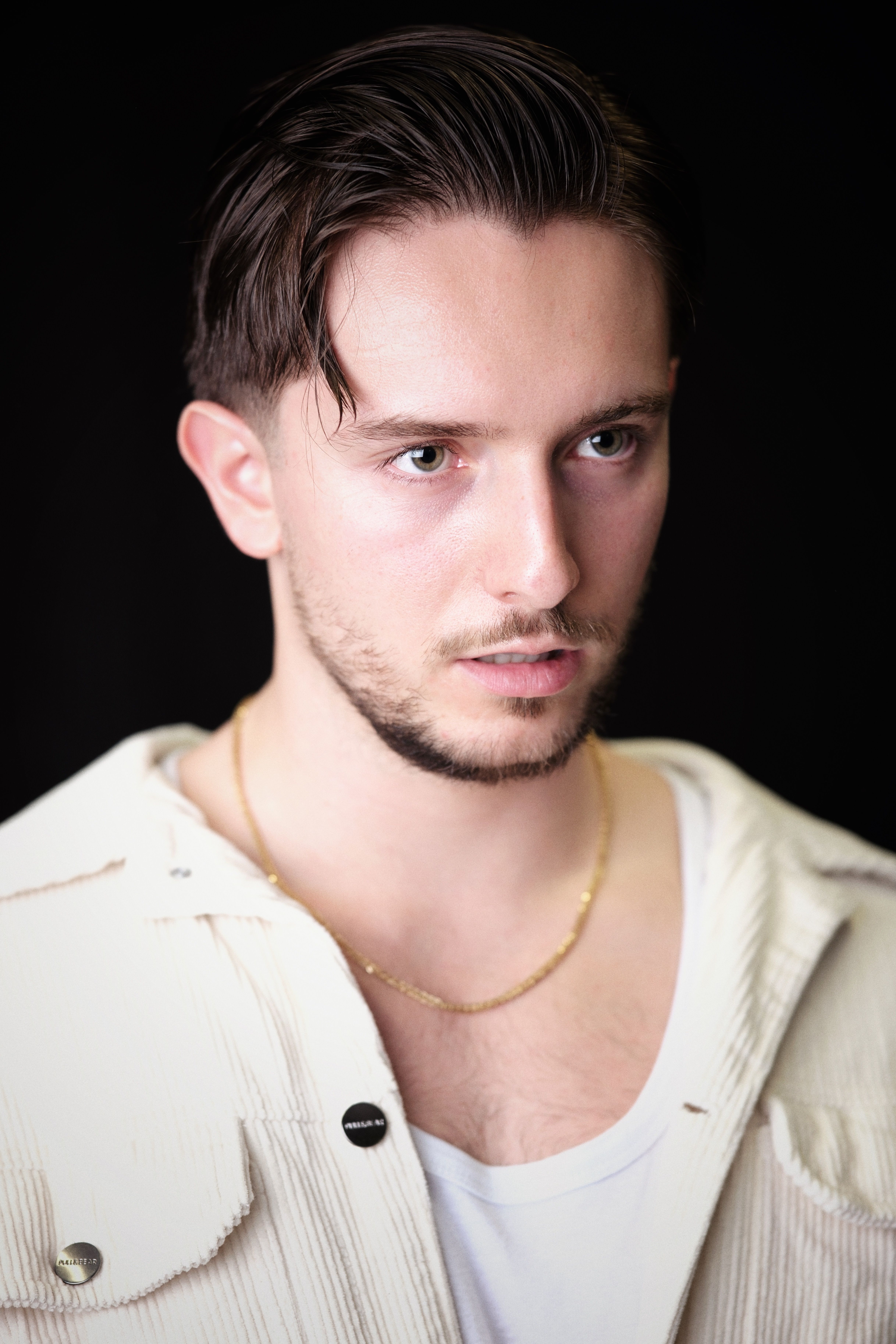 Portrait of a young man in a white jacket against a dark background.