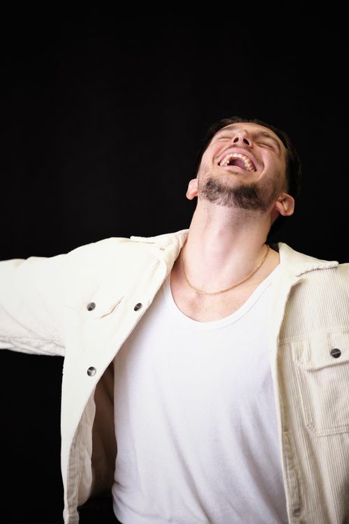 Free A young man in a white jacket laughs joyfully against a dark background. Stock Photo