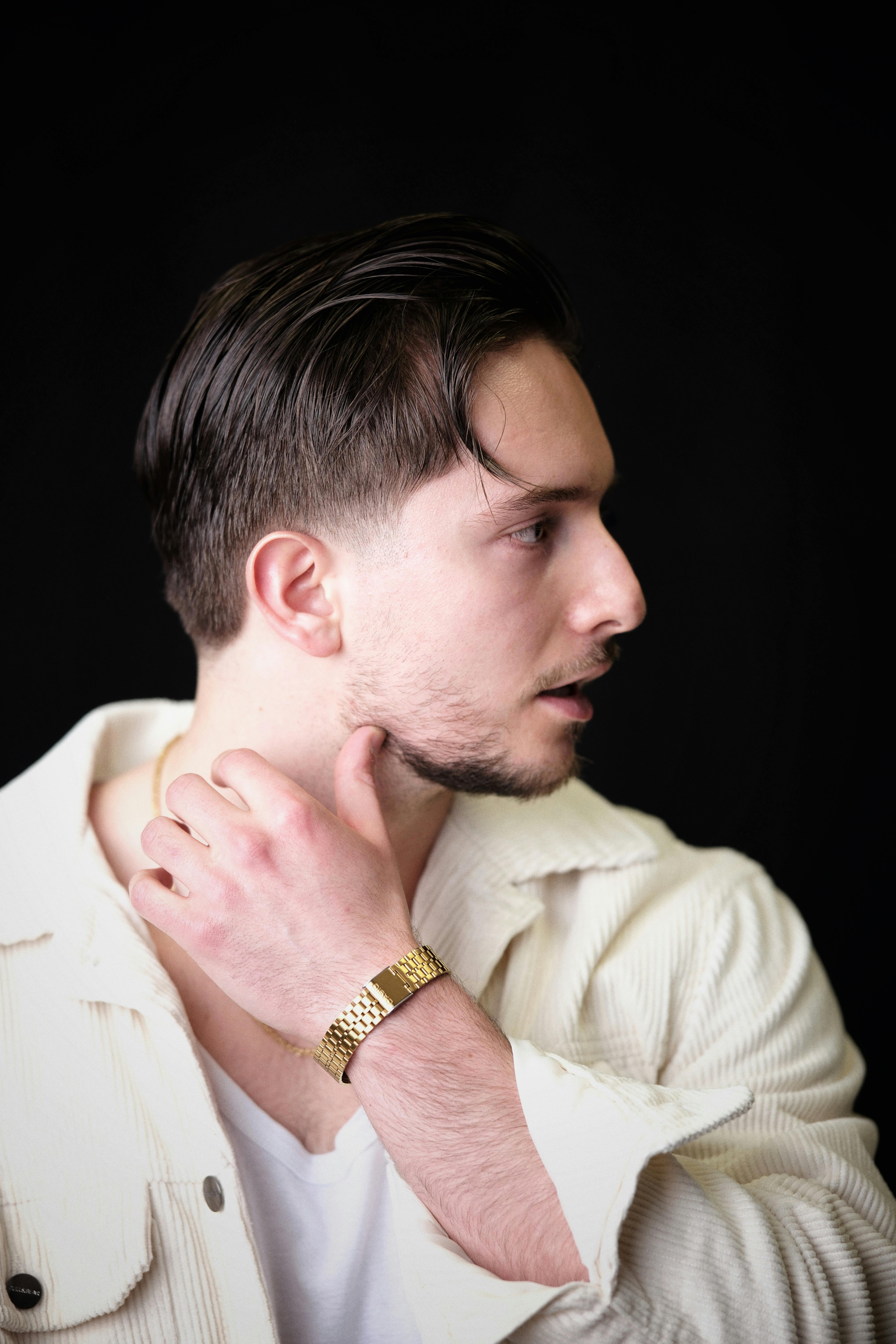 Free Profile portrait of a stylish young man with gold watch in a white jacket against a black background. Stock Photo