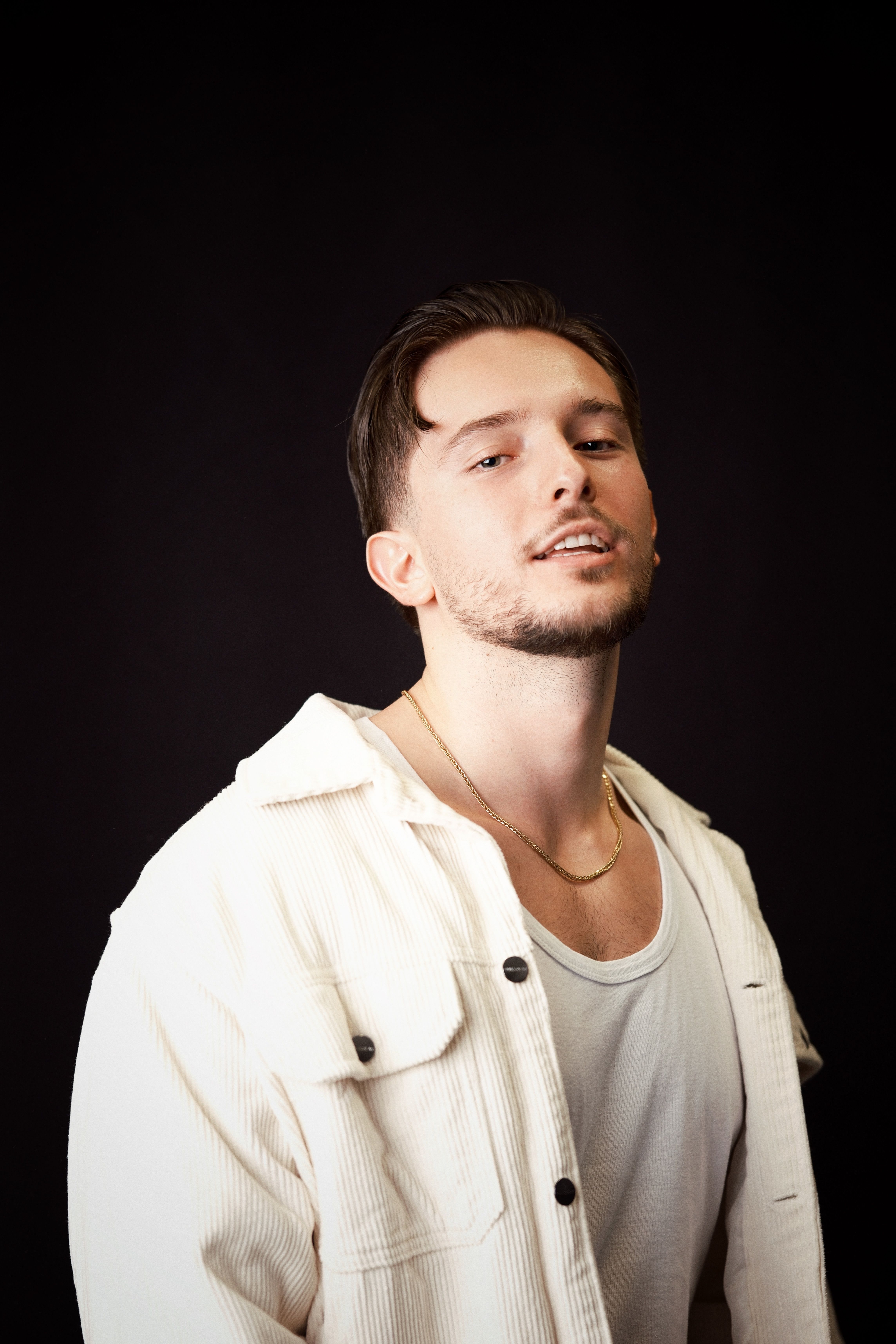 Portrait of a young man in a white jacket against a dark background, exuding confidence.