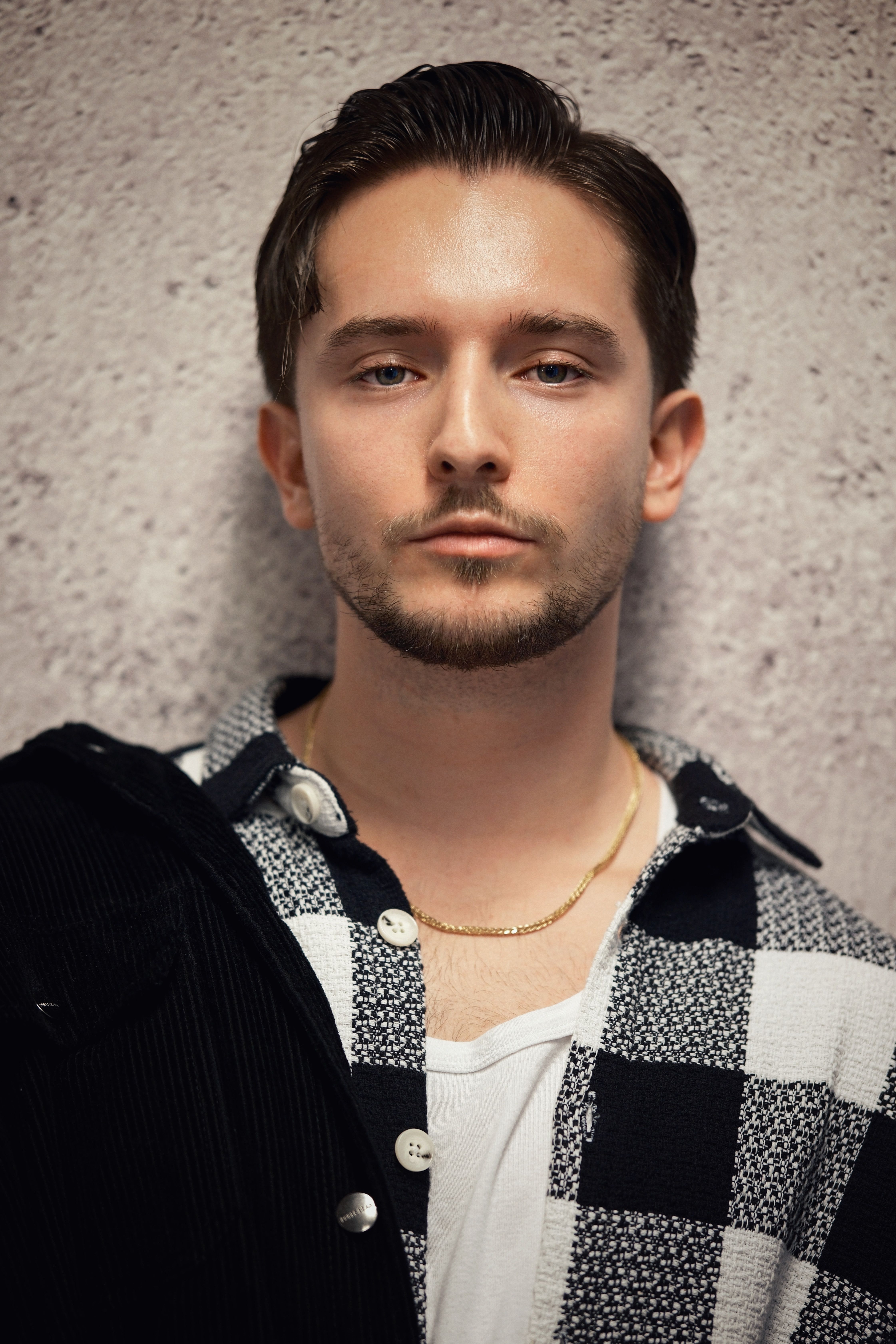 Stylish young man posing confidently against a textured wall.