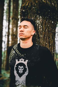 A man calmly rests against a tree, eyes closed, in a peaceful pine forest setting.