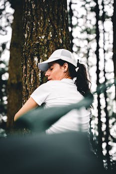 A young woman in a white cap embraces a tree in a serene forest, promoting nature connection.
