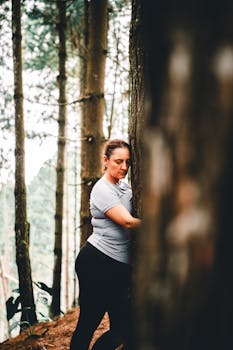 Woman embraces tree in peaceful forest setting, enjoying nature's tranquility.