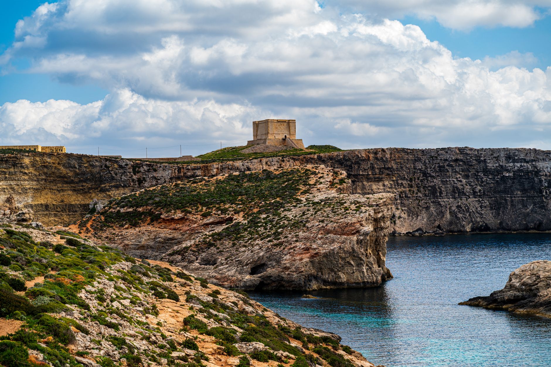 Explore Malta's rugged beauty with scenic cliffs and Fort St. Mary under a cloudy sky.