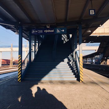 Sunlit train station platform with a shadow cast on the staircase and directional signs overhead.