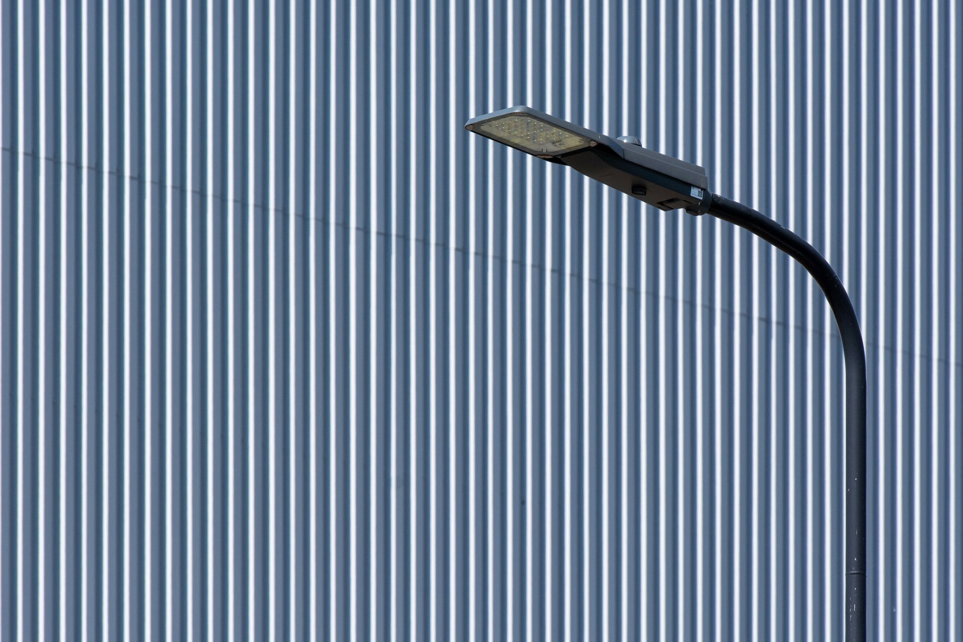 A sleek LED street light stands in front of a vertically striped industrial wall, emphasizing modern urban design.