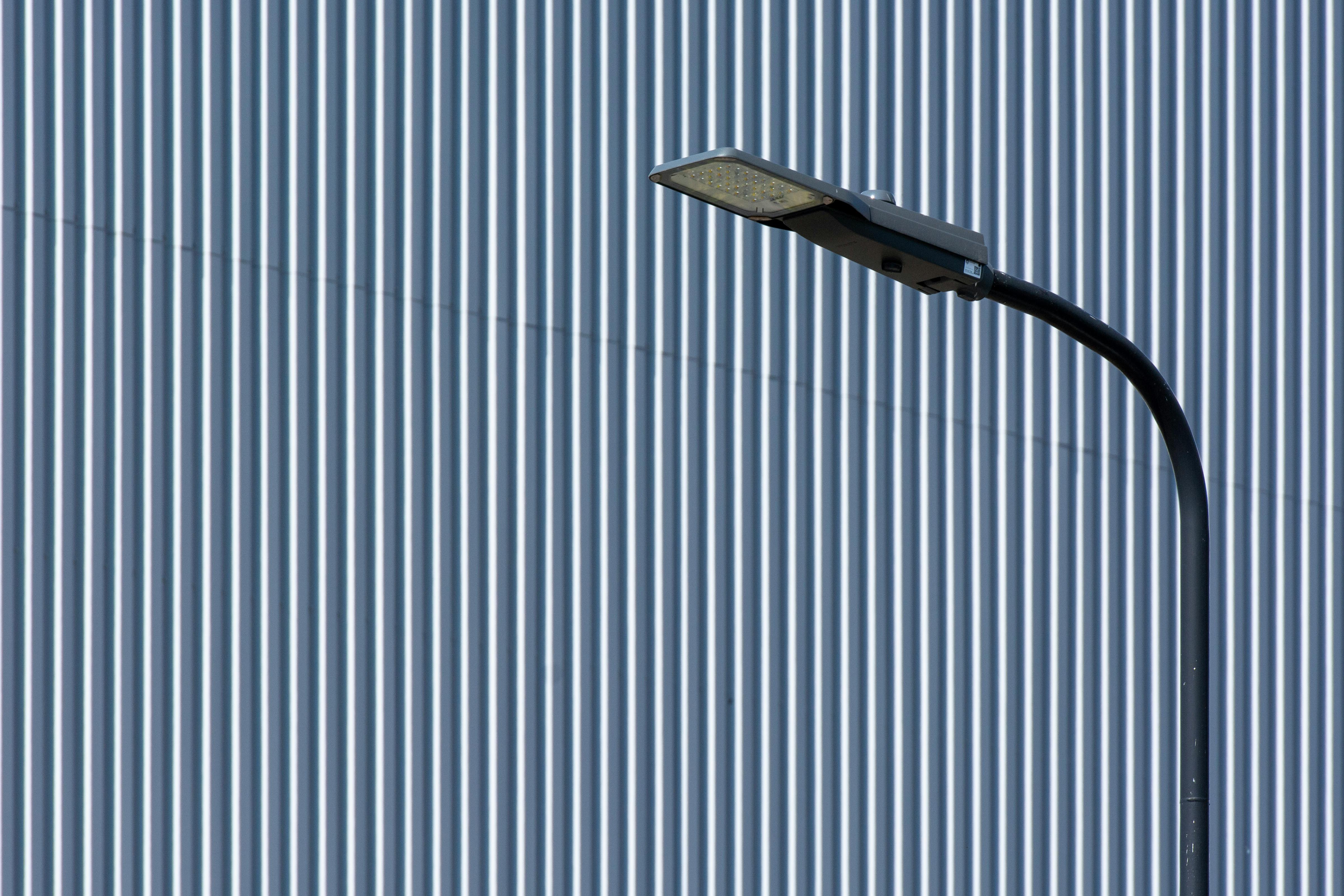 무료 수직 줄무늬 산업용 벽 앞에 세련된 LED 가로등이 세워져 있어 현대적인 도시 디자인을 강조하고 있습니다. 스톡 사진