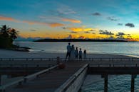 一家人站在海滩码头上，一起观看充满活力的热带日落