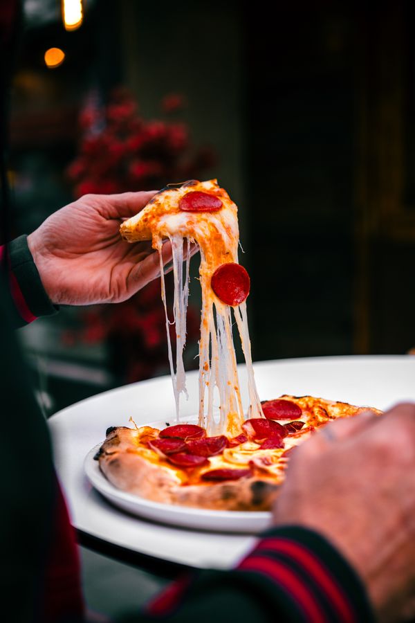 Hand lifting a pizza slice with stretching cheese
