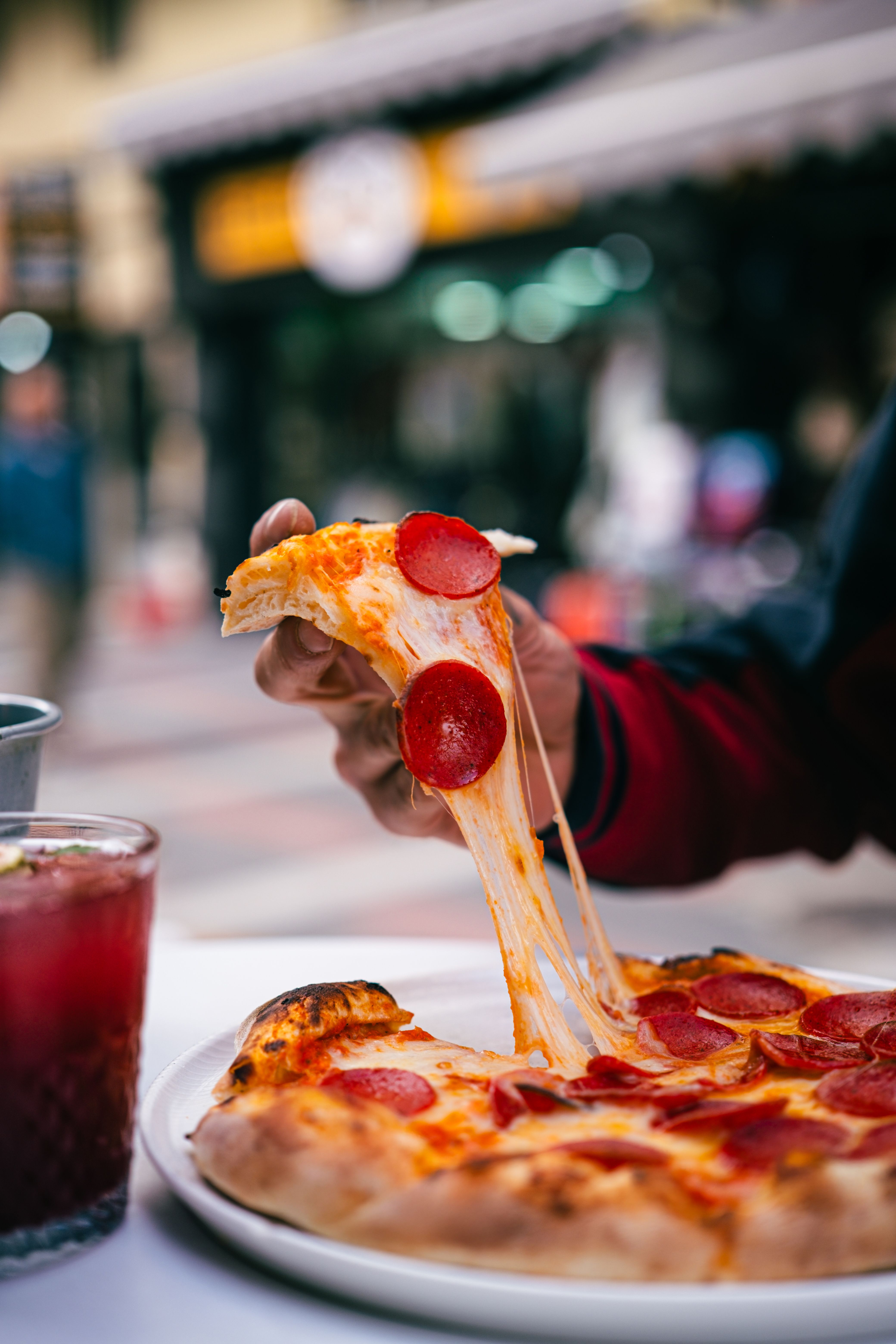 Delicious pepperoni pizza slice being pulled with gooey cheese, paired with a refreshing drink outdoors.