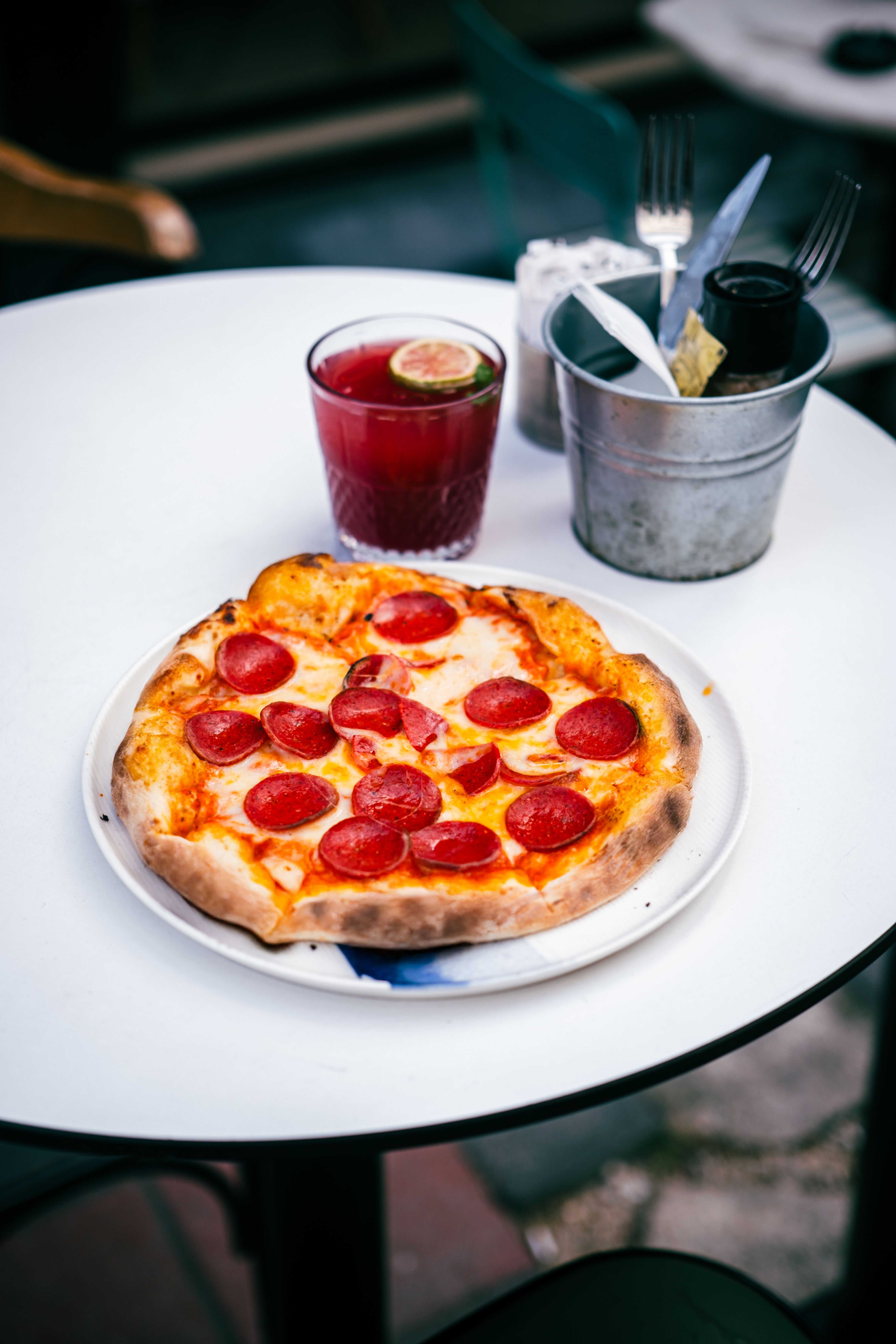Delicious pepperoni pizza served on an outdoor cafe table with a refreshing drink.