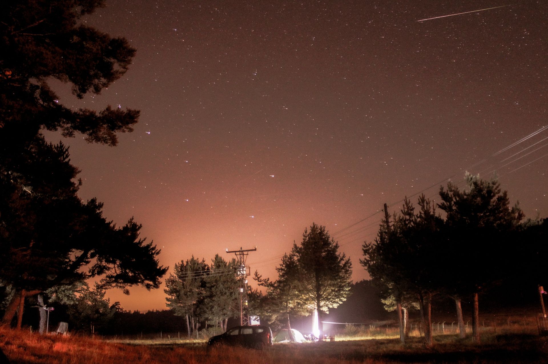 A serene night camping scene with a starry sky and meteor streak above a forest.