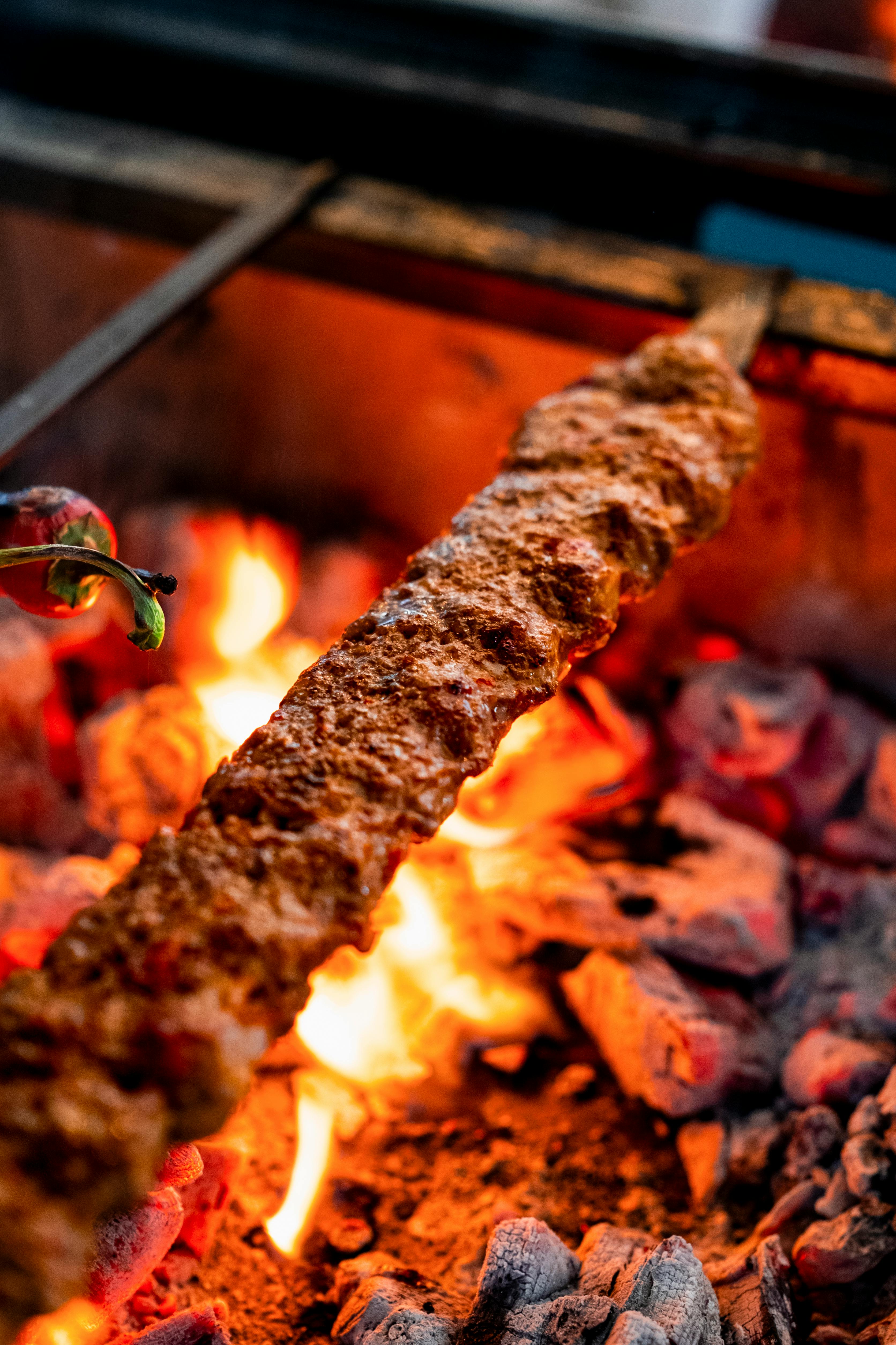 Grilled Adana kebab on metal skewer showing charred exterior with visible red pepper spices