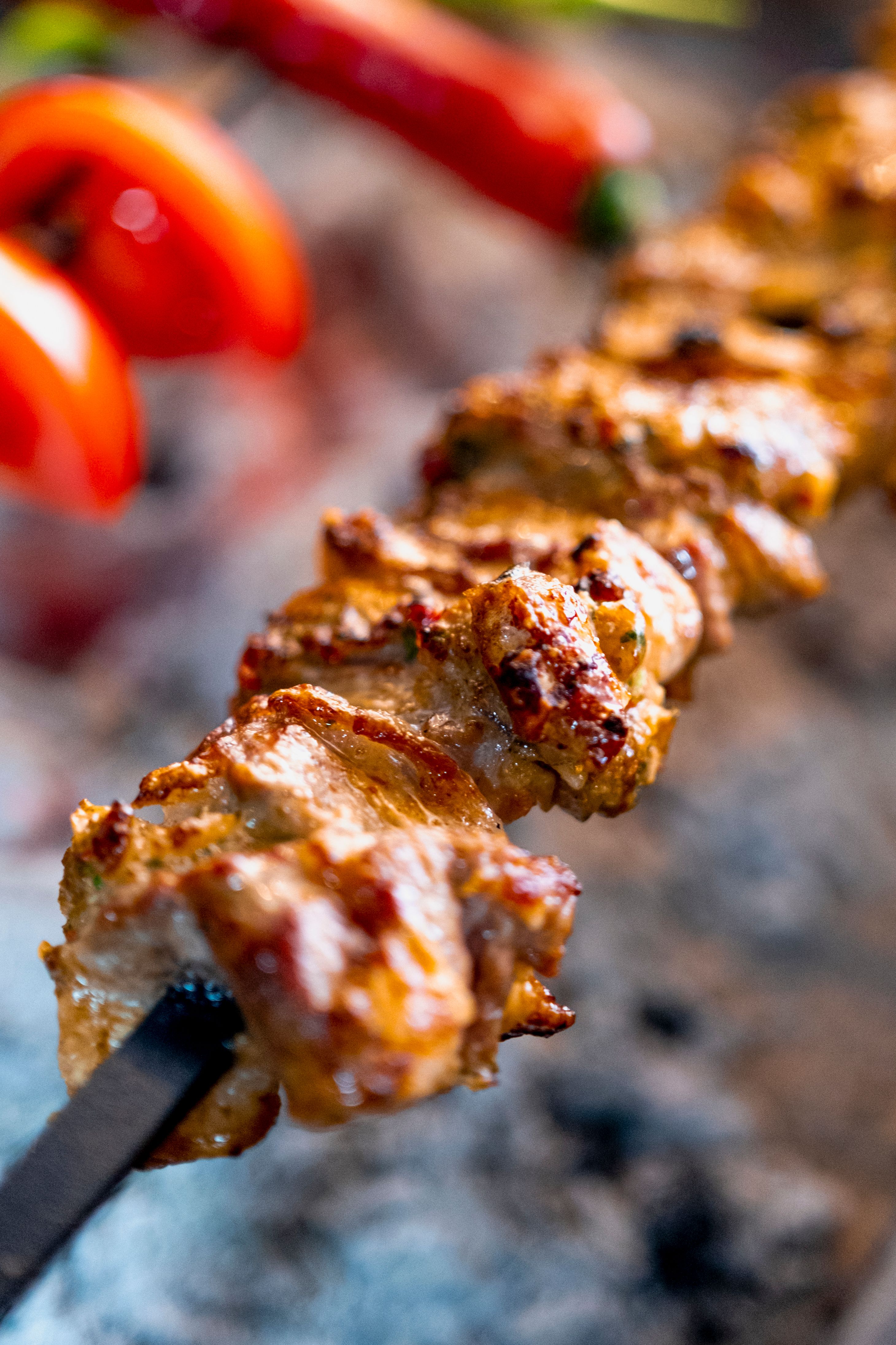 Juicy marinated chicken skewer sizzling on the grill with vibrant vegetables in the background.