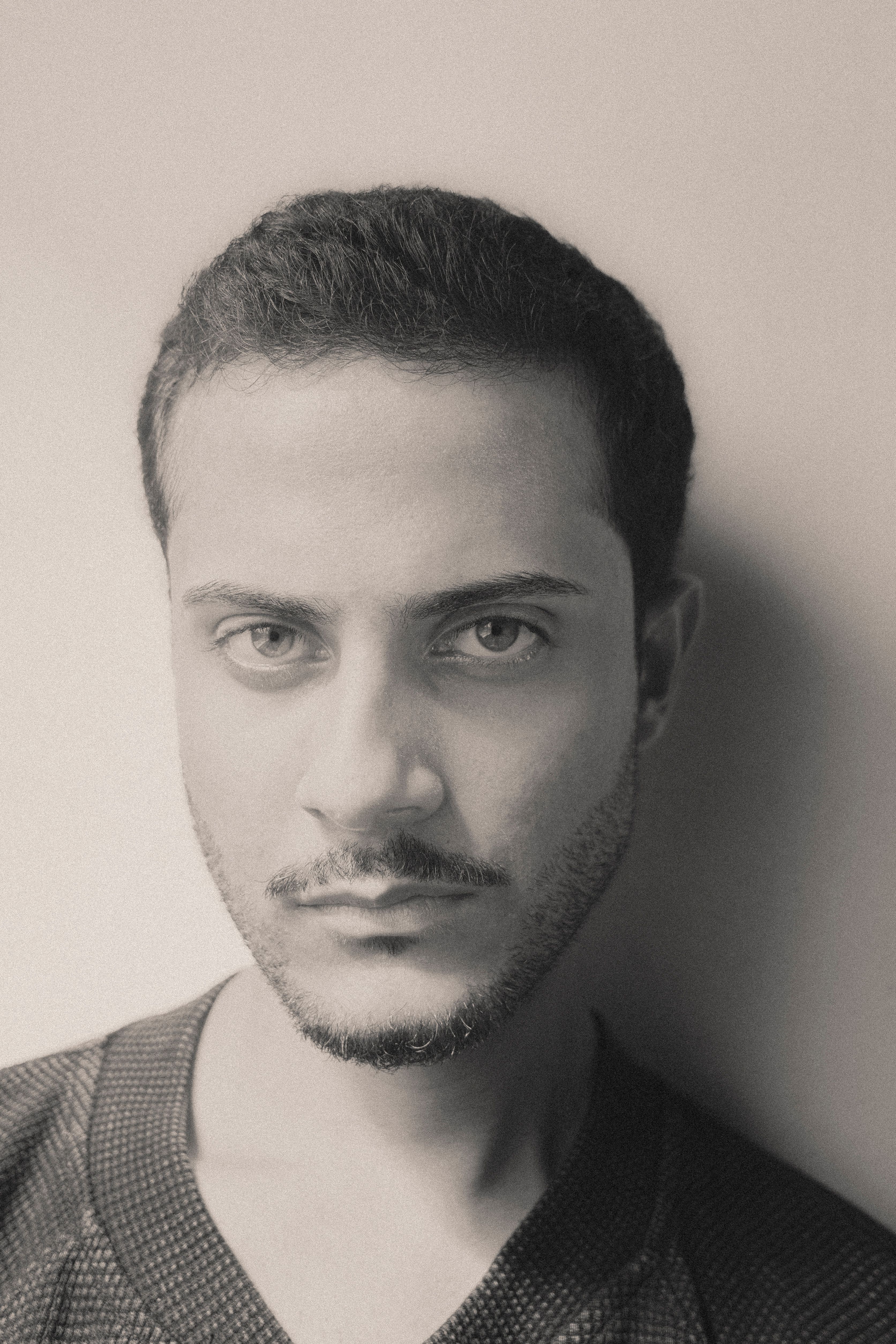 Close-up monochrome portrait of a young adult man looking thoughtfully at the camera.