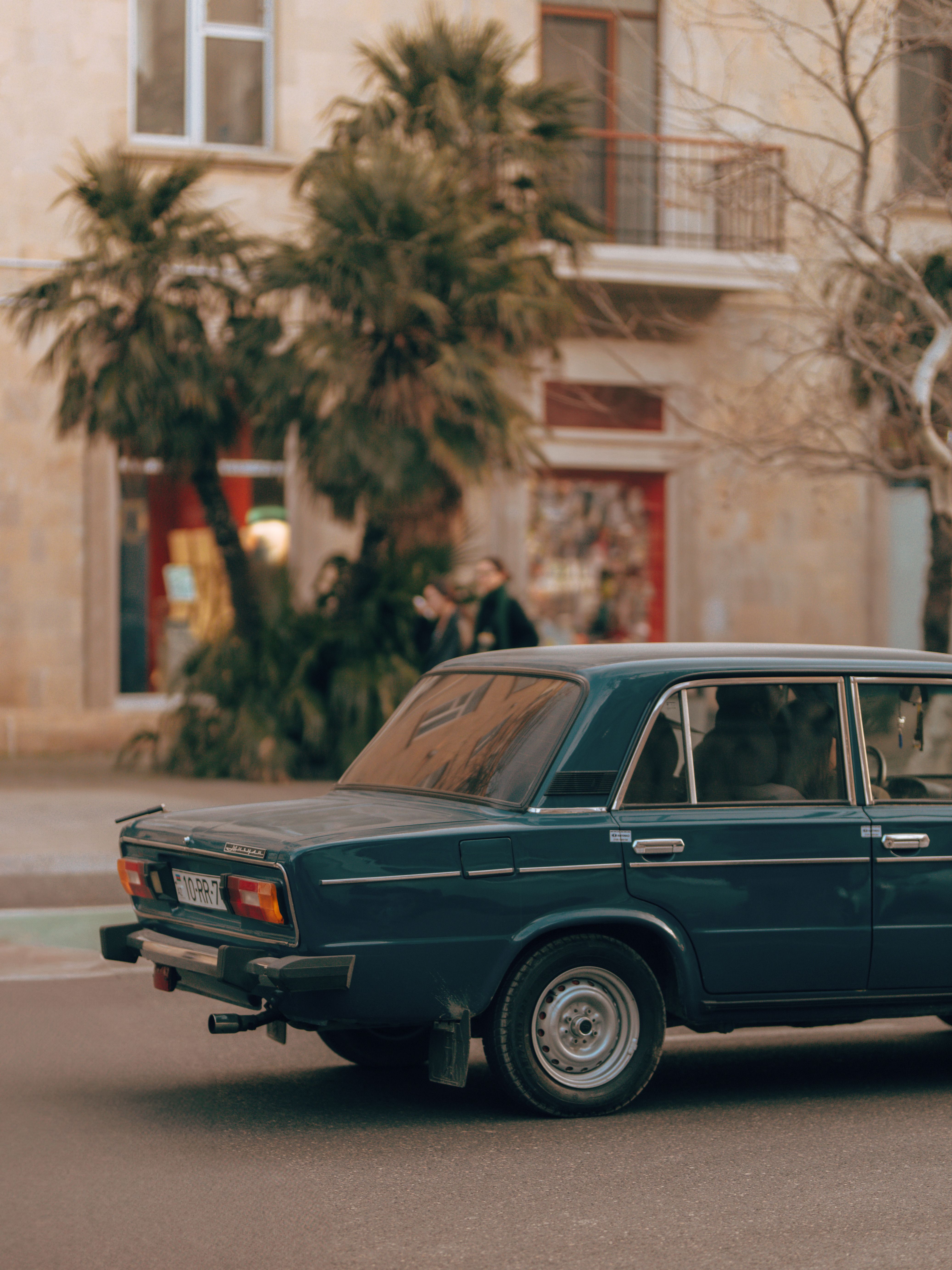 Fotomural Coche clásico vintage aparcado en una calle urbana con palmeras y edificios.