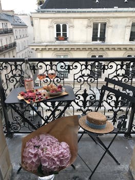 Cozy Parisian balcony setup with wine, snacks, and flowers on a sunny day.