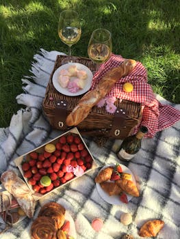 A summer picnic setup featuring baguettes, strawberries, croissants, wine, and macarons on a blanket.