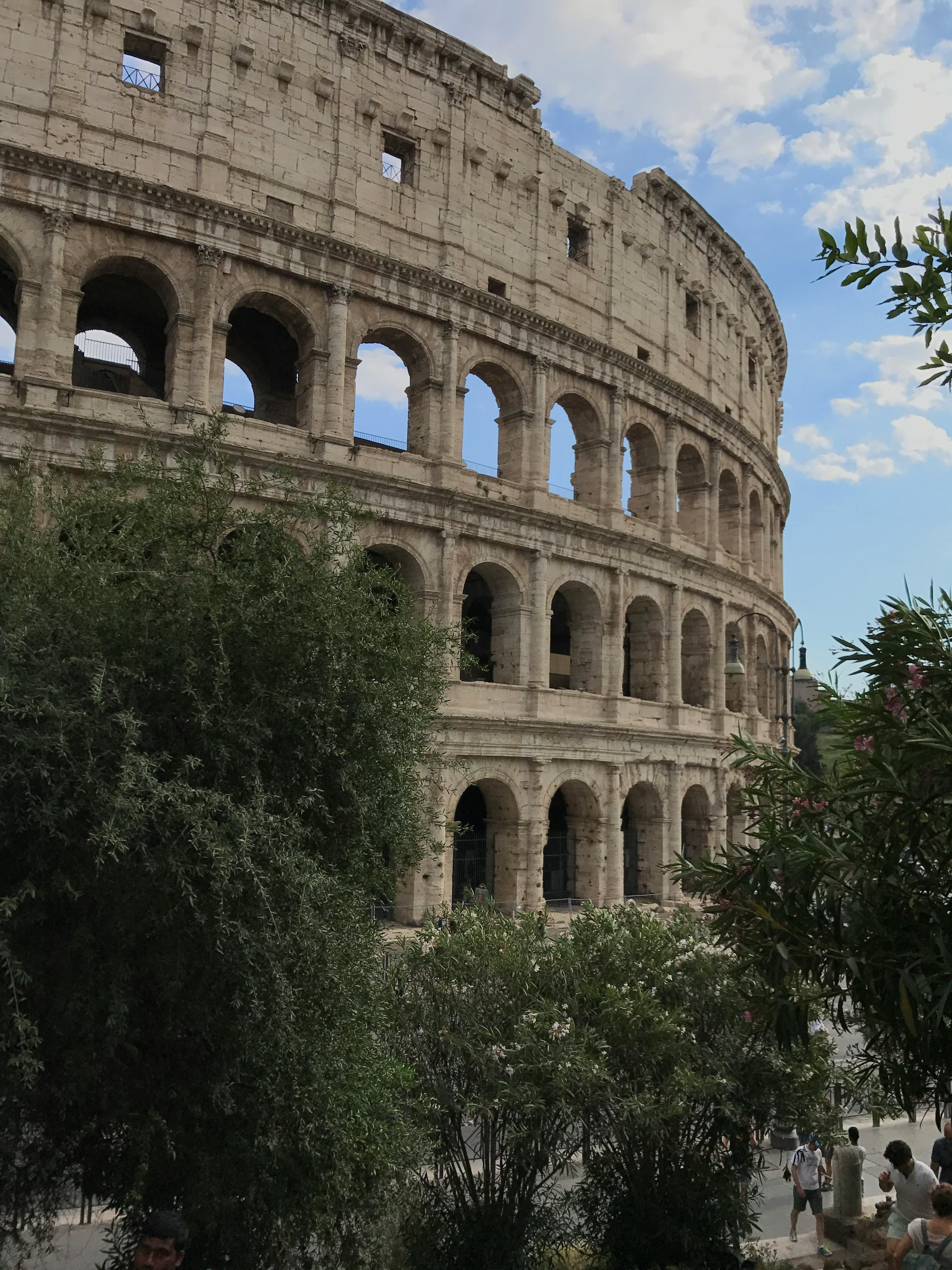 Gratis Historisk Colosseum i Roma fanget i dagslys med omkringliggende grøntområder. Ikonisk landemerke. Arkivbilde